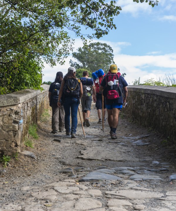 Eine Gruppe von Pilgern überquert die mittelalterliche Brücke von Furelos, Spanien, © MIMOHE – stock.adobe.com